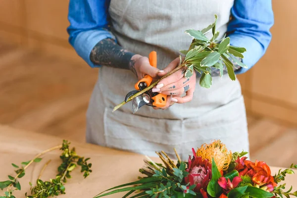 Mid section of young florist in apron cutting plants at workplace — Stock Photo