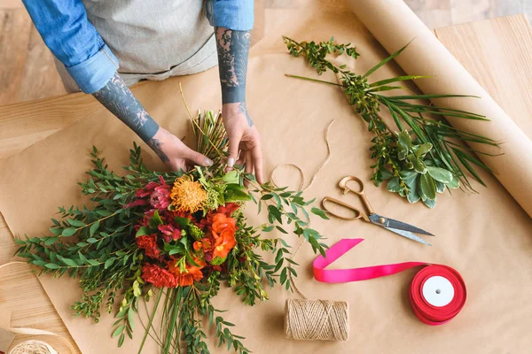 Abgeschnittene Aufnahme eines Blumenhändlers mit tätowierten Händen, der schöne Blumen zu einem Strauß arrangiert — Stockfoto