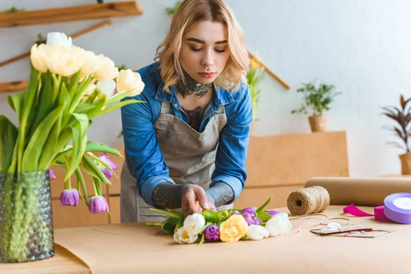 Молодой флорист работает с красивыми цветами тюльпана на рабочем месте — стоковое фото
