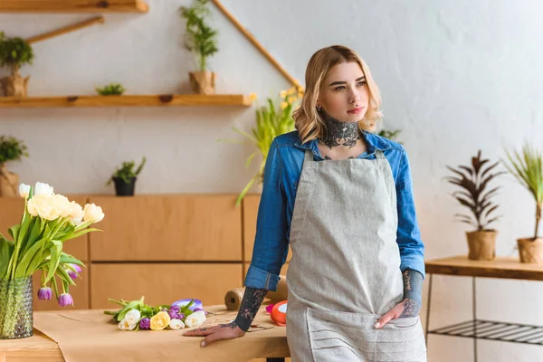 Junge Floristin lehnt an Tisch und schaut im Blumenladen weg — Stockfoto