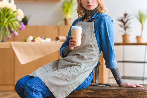 Foto recortada de florista en delantal sosteniendo café para llevar - foto de stock