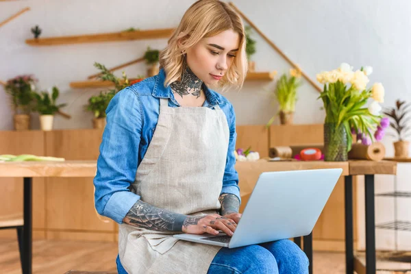 Florista joven en delantal usando el ordenador portátil en la tienda de flores — Stock Photo