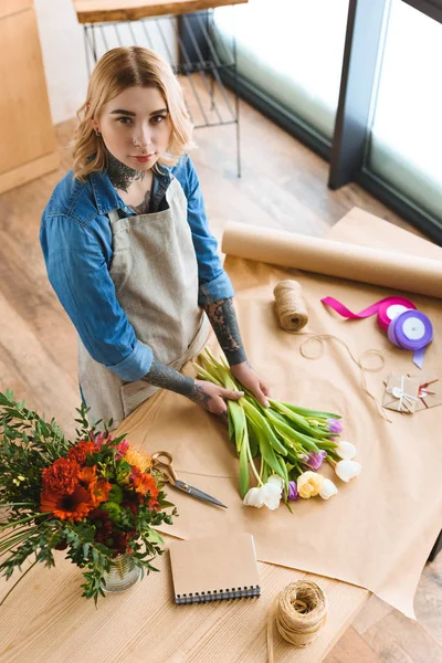 High angle view of young florist arranging flowers and looking at camera — Stock Photo
