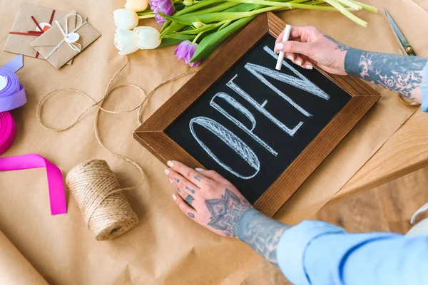 Abgeschnittene Aufnahme eines jungen tätowierten Blumenhändlers, der Wort offen an Bord schreibt — Stockfoto