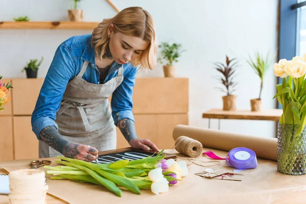 Florista joven en delantal palabra de escritura abierta a bordo en la tienda de flores - foto de stock