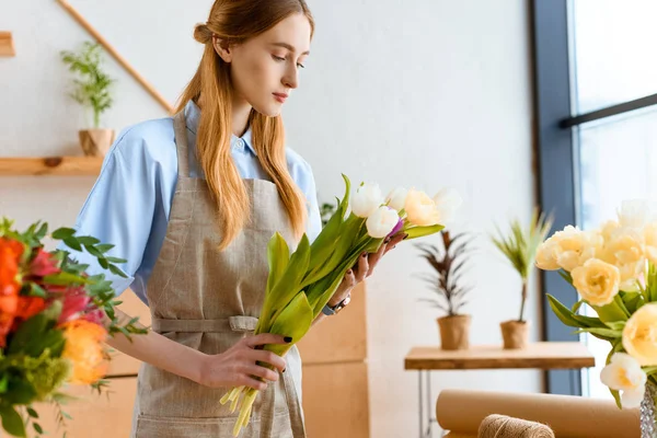 Young florist in apron holding beautiful tulips in flower shop — Stock Photo