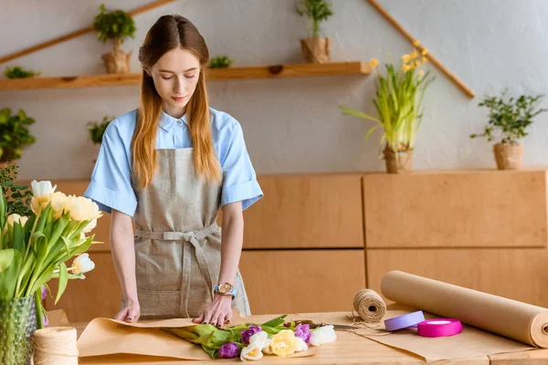 Schöne junge Floristin wickelt Blumenstrauß am Arbeitsplatz ein — Stockfoto