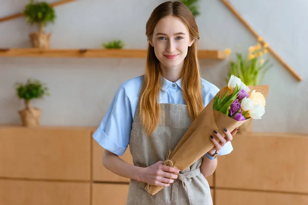 Schöne junge Floristin hält einen Strauß Tulpen und lächelt in die Kamera — Stockfoto