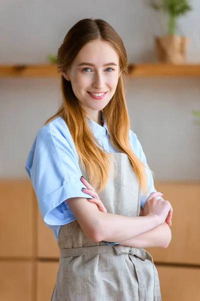 Belle jeune fleuriste debout avec les bras croisés et souriant à la caméra — Photo de stock