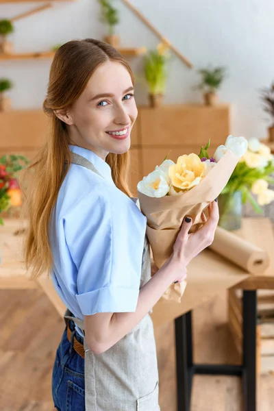 Junge Floristin hält schönen Strauß Tulpen in der Hand und lächelt in die Kamera im Blumenladen — Stockfoto