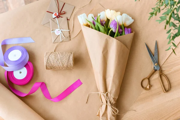 Vista dall'alto di un bellissimo bouquet di tulipani, forbici, nastri e buste con corda su carta artigianale — Foto stock