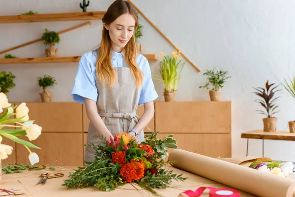 Junge Floristin in Schürze arrangiert Blumenstrauß am Arbeitsplatz — Stockfoto