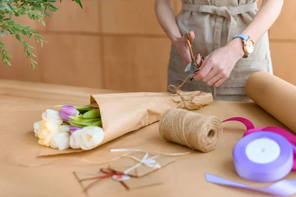 Cropped shot of florist in apron arranging bouquet of tulips in craft paper — Stock Photo