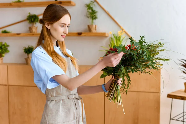 Beautiful smiling young female florist in apron holding bouquet of flowers — Stock Photo