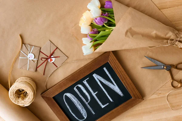 Top view of beautiful tulips, rope, scissors, envelopes and open sign on craft paper — Stock Photo