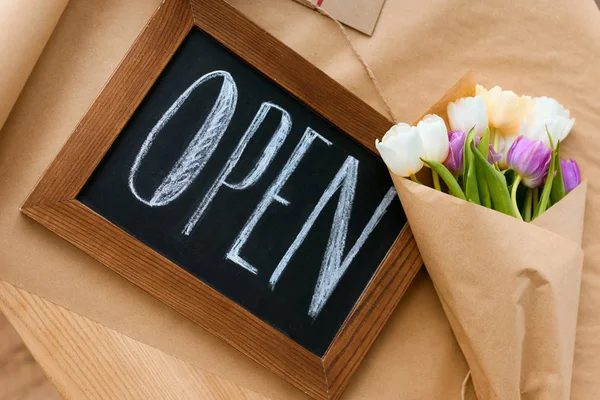 Vue de dessus de beau bouquet de tulipes et panneau ouvert sur papier artisanal — Photo de stock