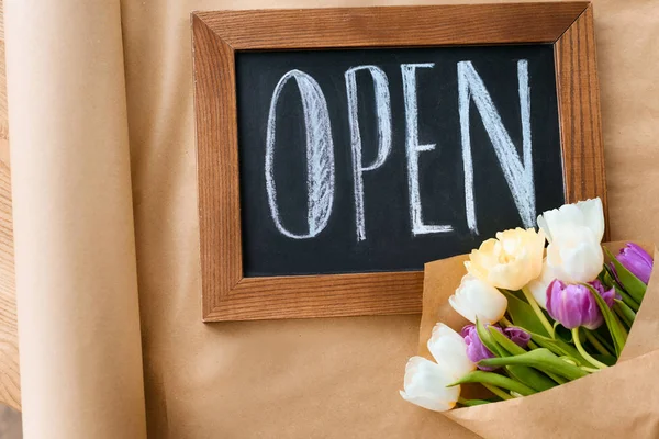 Top view of beautiful tulips and open sign on craft paper — Stock Photo
