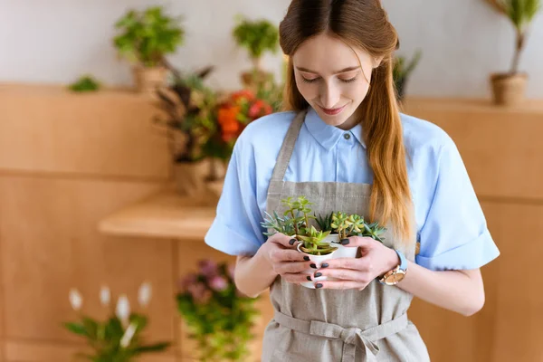 Bela sorridente jovem florista segurando suculentas em vasos na loja de flores — Fotografia de Stock