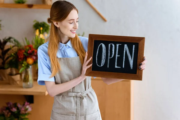 Beautiful smiling young florist holding sign open in flower shop — Stock Photo