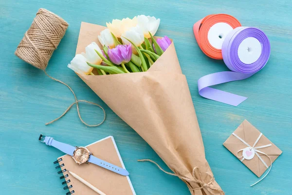 Top view of beautiful tulips in craft paper, rope, ribbons, envelope and notebook with wristwatch — Stock Photo