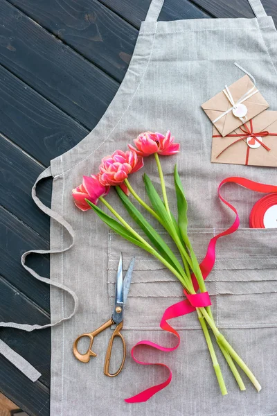 Hermosas flores de tulipán con sobres, cinta y tijeras en delantal - foto de stock