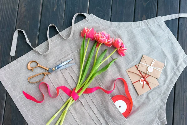 Top view of beautiful tulips with envelopes, ribbon and scissors on apron — Stock Photo