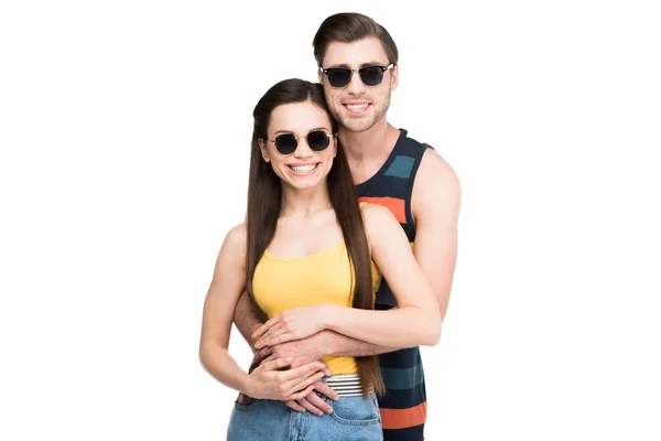 Pareja alegre en gafas de sol abrazando y mirando a la cámara, aislado en blanco - foto de stock