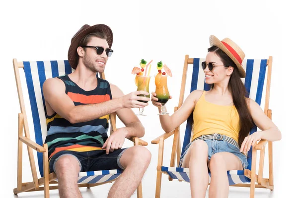 Glückliches Paar auf Liegestühlen und klirrenden Gläsern mit Cocktails, isoliert auf weiß — Stockfoto