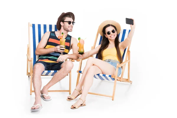 Casal relaxante em cadeiras de praia com coquetéis e tomar selfie, isolado em branco — Fotografia de Stock