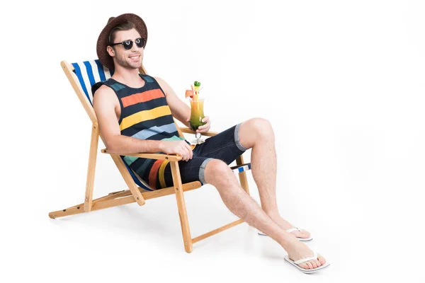 Bel homme en lunettes de soleil et chapeau relaxant sur chaise de plage avec cocktail, isolé sur blanc — Photo de stock