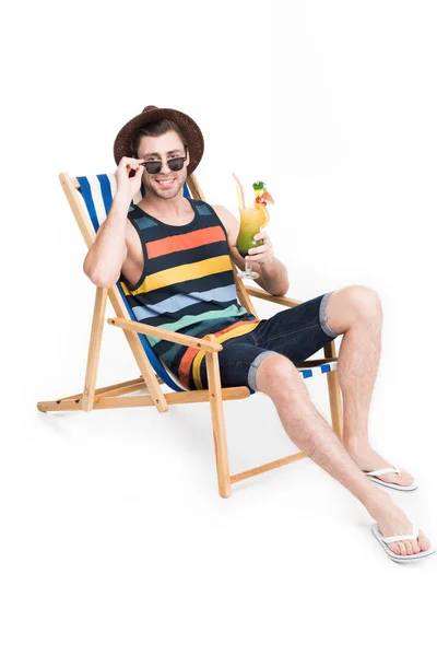 Hombre en gafas de sol y sombrero relajante en silla de playa con cóctel, aislado en blanco - foto de stock