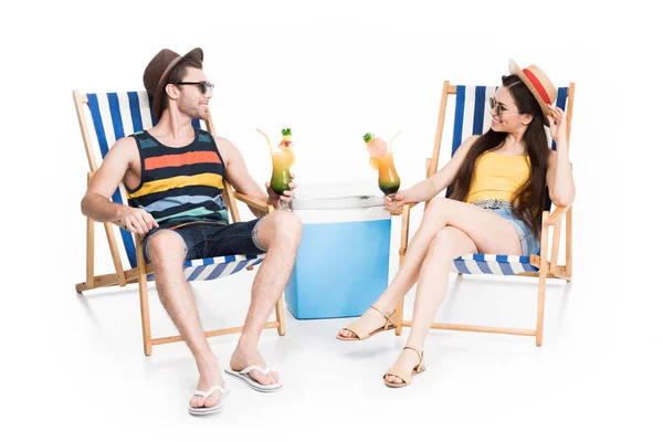 Casal relaxante em cadeiras de praia com coquetéis e refrigerador caixa, isolado em branco — Fotografia de Stock