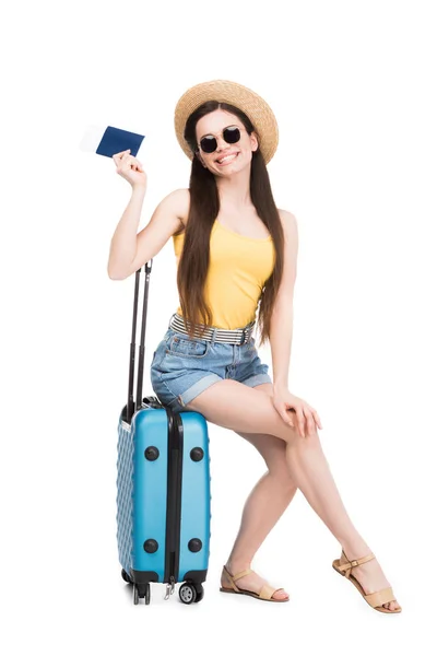 Pretty smiling girl with passport, air ticket sitting on travel bag, isolated on white — Stock Photo