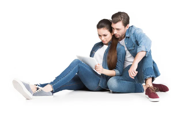 Пара в джинсовой сидя и используя планшет, изолированные на белом — стоковое фото