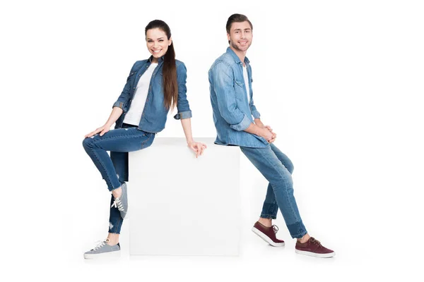 Happy couple in denim leaning on white cube, isolated on white — Stock Photo