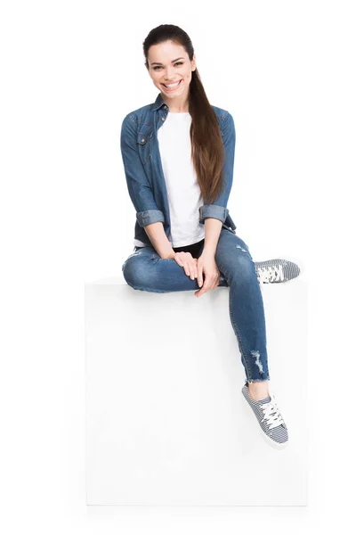 Attractive brunette woman sitting on white cube, isolated on white — Stock Photo
