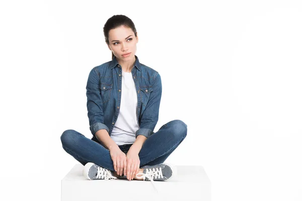 Jovem mulher bonita em jeans sentado no cubo branco, isolado no branco — Fotografia de Stock