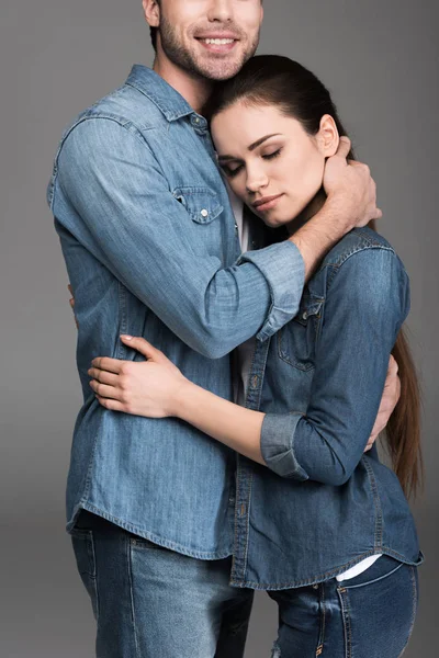Молода пара в джинсовому одязі, обіймається, ізольована на сірому — стокове фото