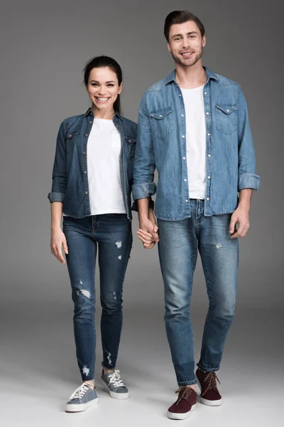 Feliz pareja cogida de la mano y mirando a la cámara, en gris — Stock Photo