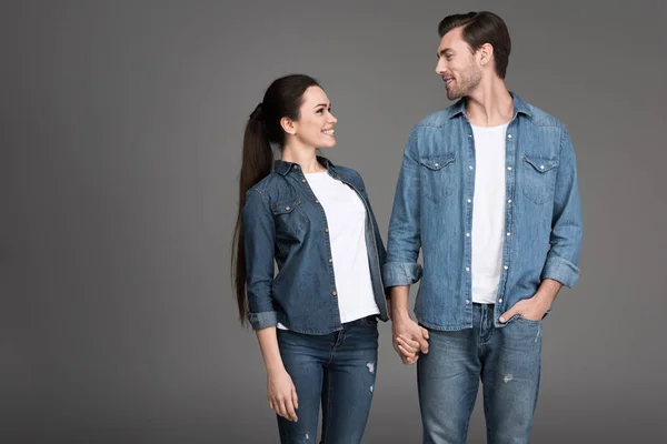 Sorrindo casal de mãos dadas e olhando um para o outro, isolado em cinza — Fotografia de Stock