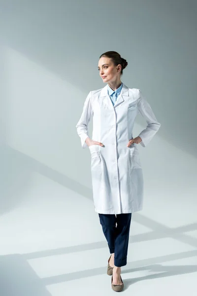 Médico fêmea grave em casaco branco olhando para longe em cinza — Fotografia de Stock