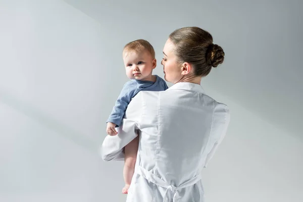 Rear view of female pediatrician holding little baby on grey — Stock Photo