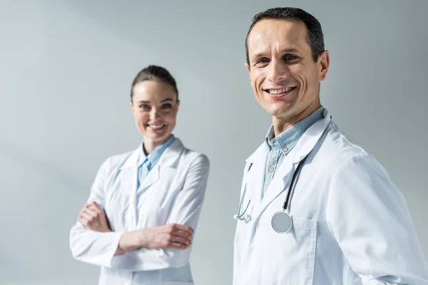 Happy adult doctors looking at camera isolated on grey — Stock Photo