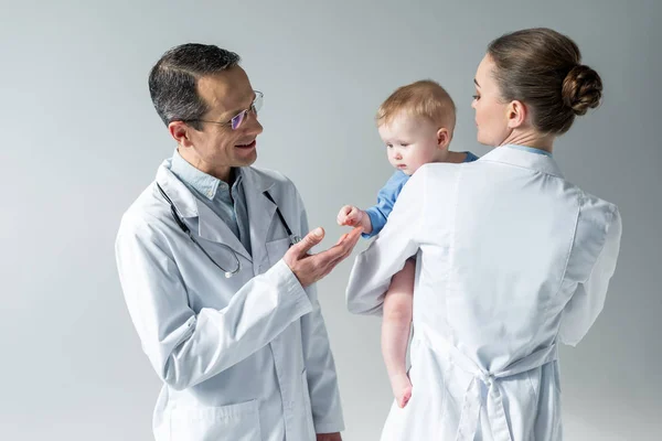 Adult pediatricians with adorable little baby on grey — Stock Photo