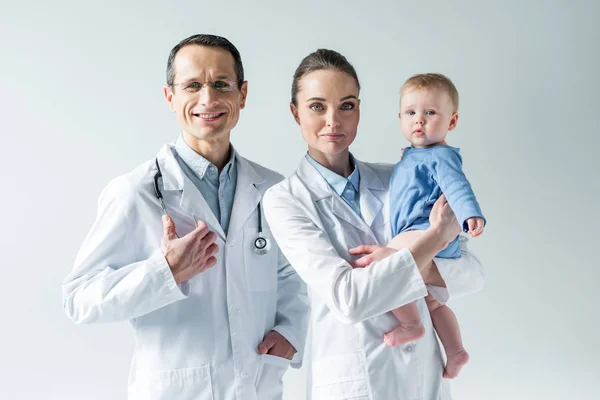 Happy adult pediatricians with little baby on grey — Stock Photo