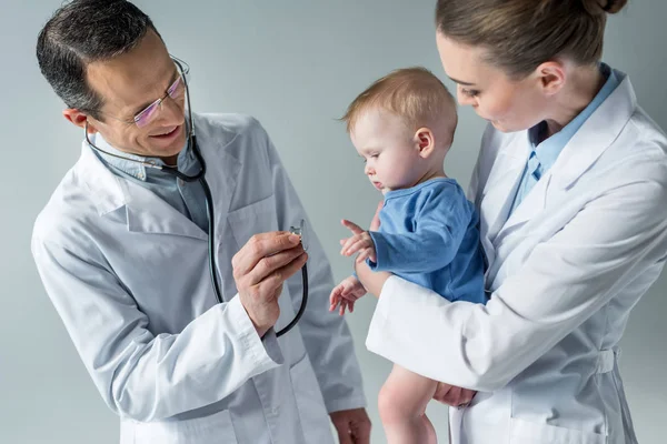 Lächelnde Kinderärzte überprüfen den Atem des entzückenden kleinen Babys — Stockfoto