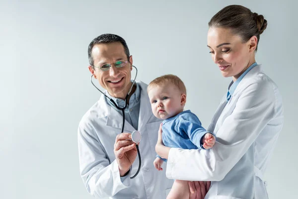 Glückliche erwachsene Kinderärzte kümmern sich um kleines Baby isoliert auf grau — Stockfoto