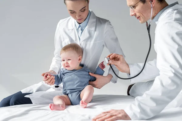 Pediatras tratando de comprobar el aliento de bebé triste en la cama - foto de stock