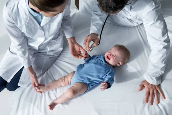 Vista de ángulo alto de los pediatras tratando de comprobar la respiración del bebé llorando - foto de stock