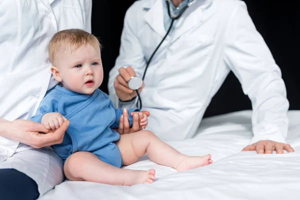 Recortado tiro de pediatras tratando de comprobar el aliento de triste bebé - foto de stock